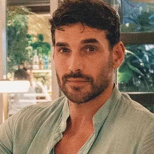 A dark-haired man with a beard in a light green shirt at a cafe.