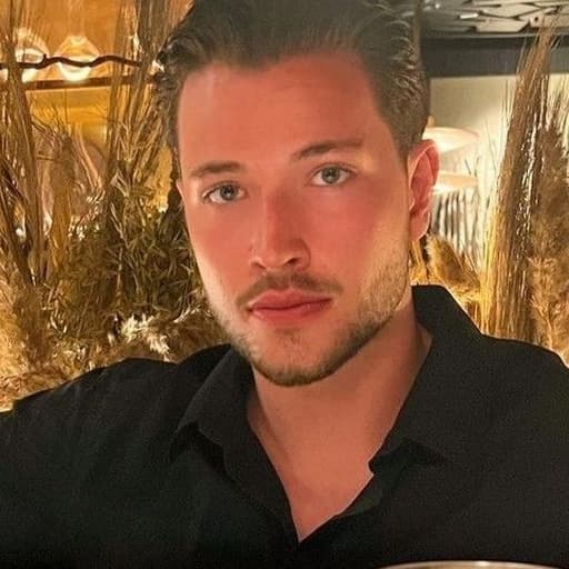An adult man with dark hair and a short beard at a warmly lit restaurant.
