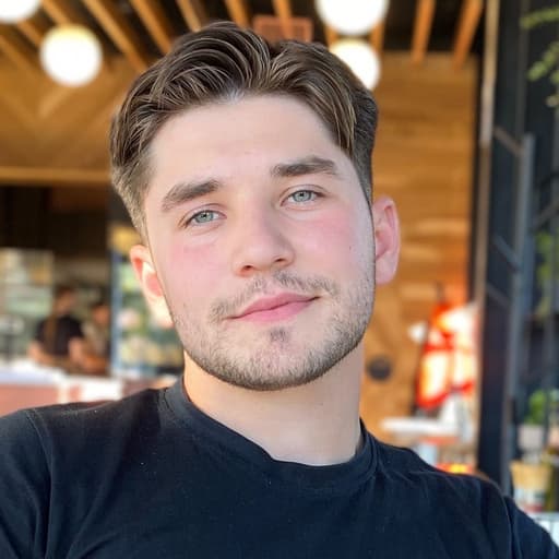 A young man in a black T-shirt seated at a cafe.