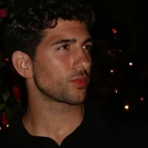 A curly-haired man in a black shirt outdoors at night.