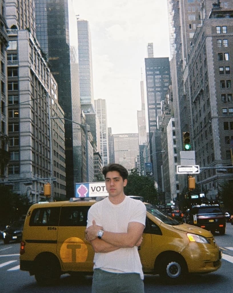 Matthew Stevens in a white T-shirt on a New York street beside a yellow cab.