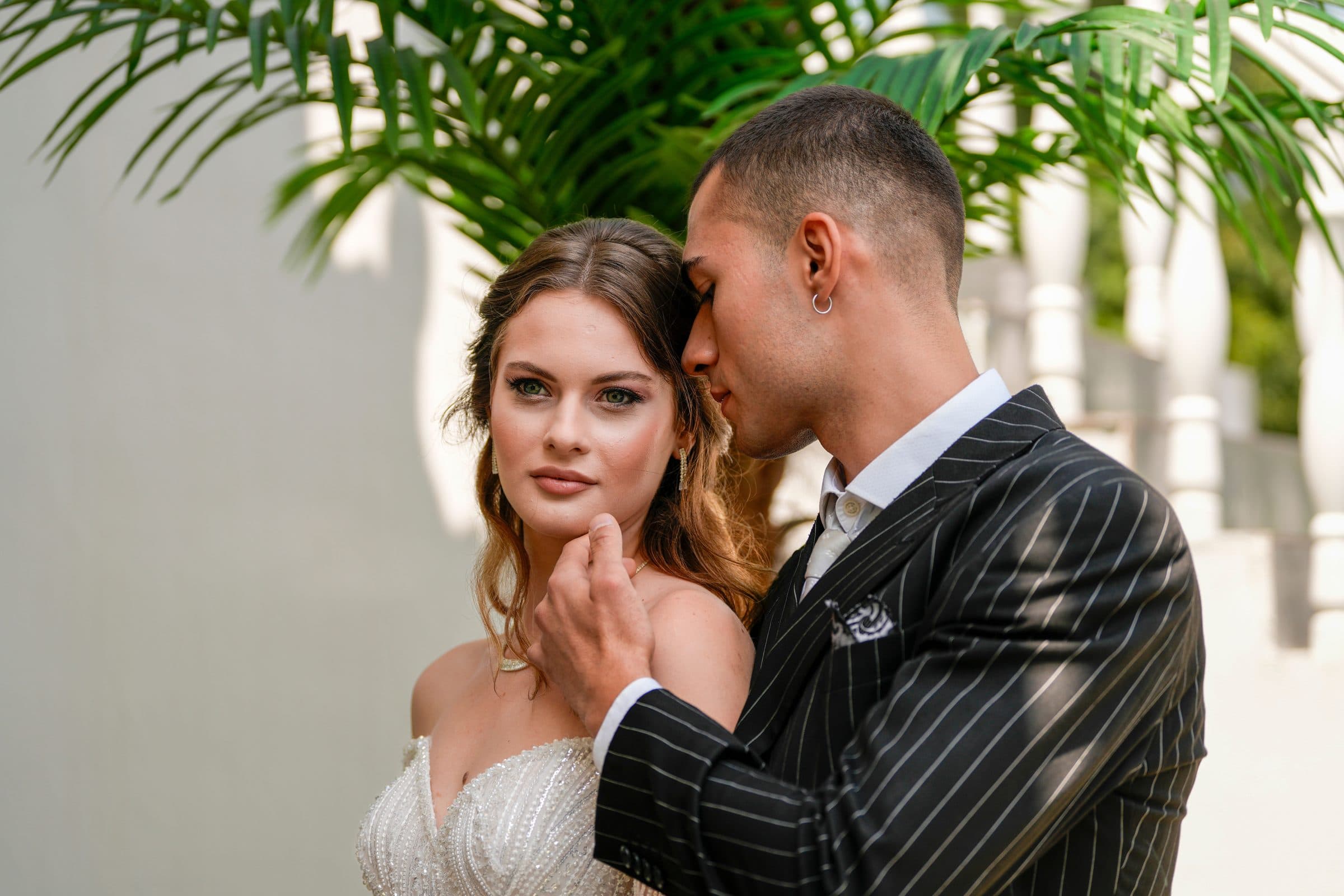 Bride in a strapless gown looking at the camera as a man in a pinstripe suit leans his head against hers