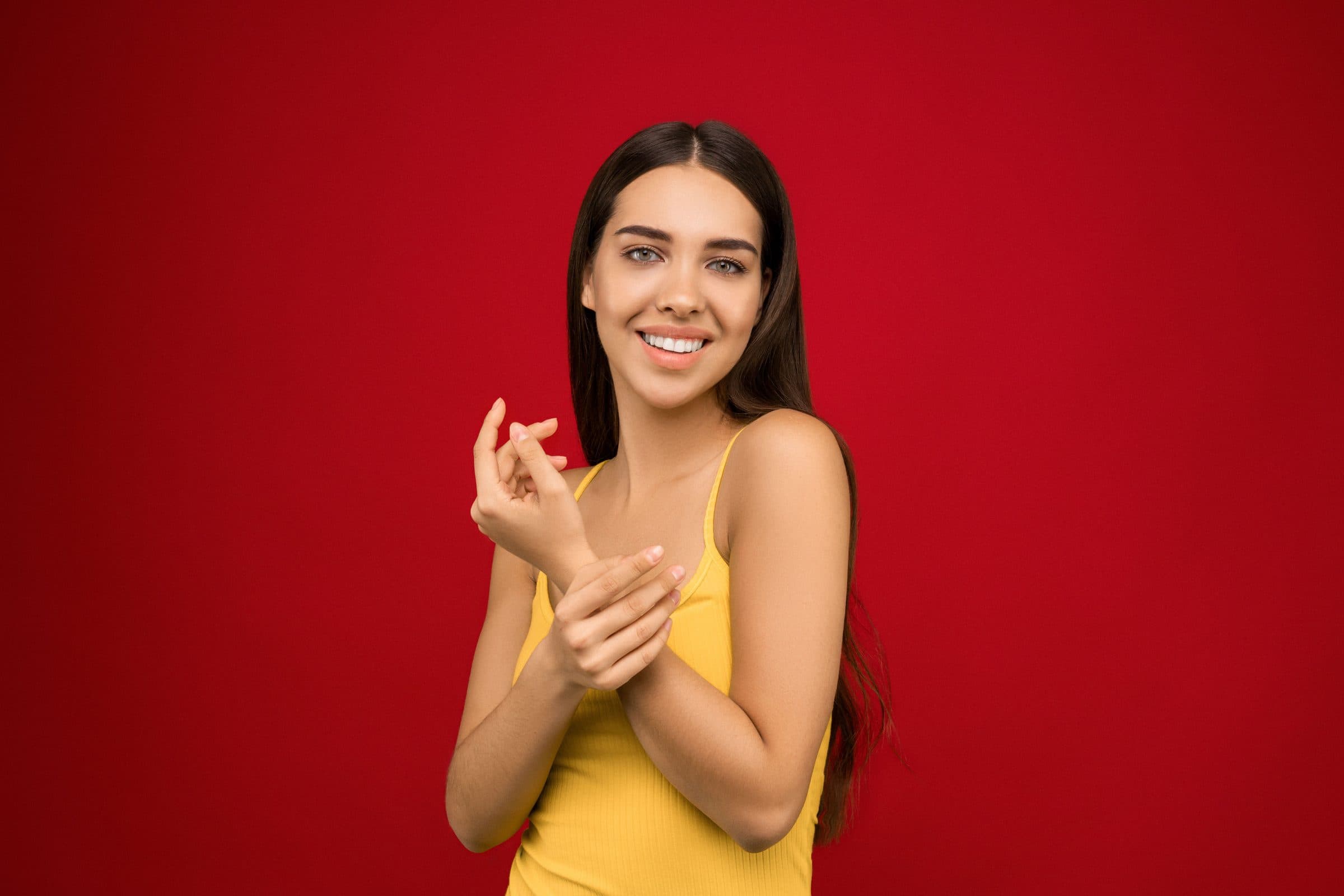 Smiling woman with long dark hair in a yellow top posing against a red backdrop