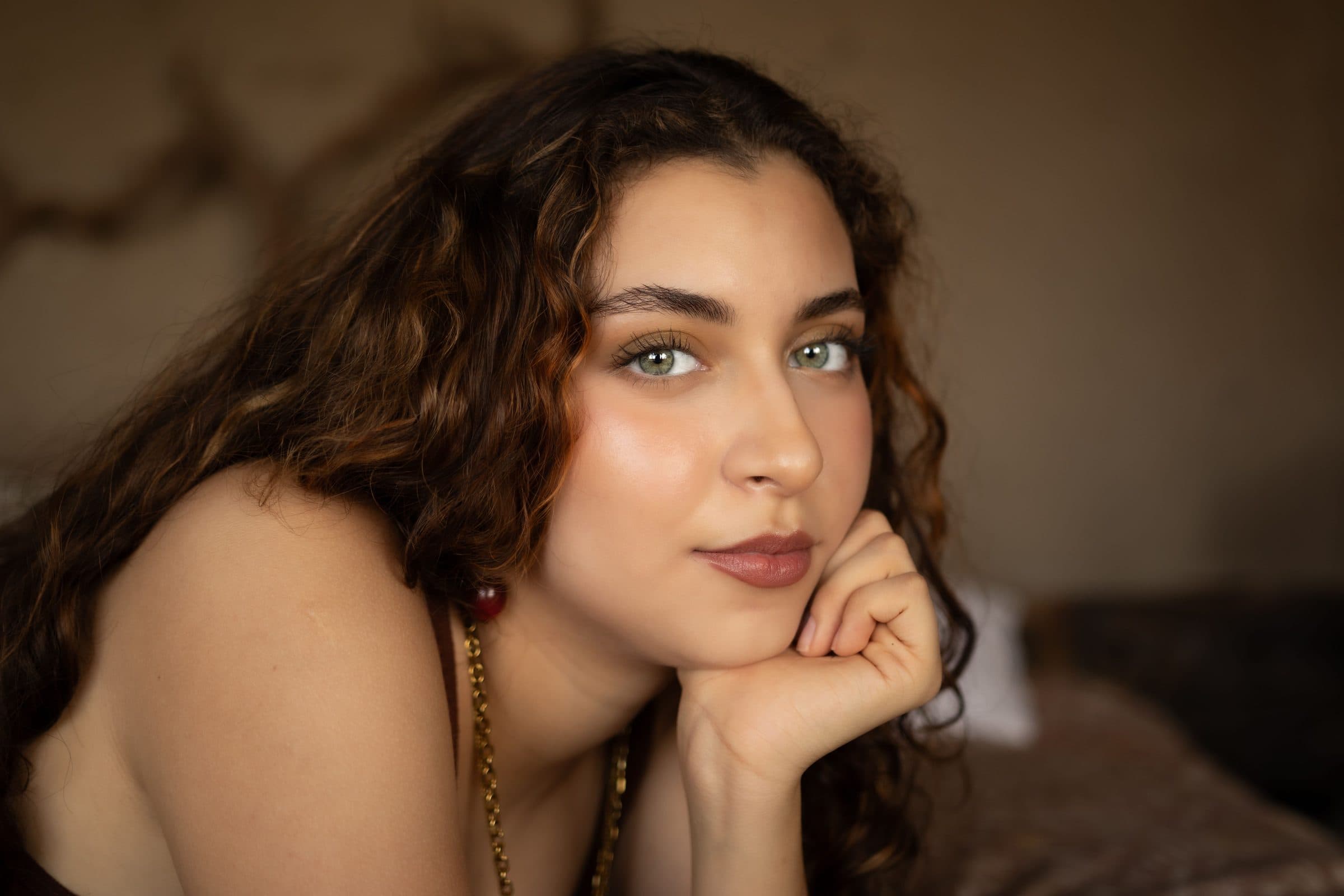 Woman with curly brown hair and green eyes resting her chin on her hand in warm light